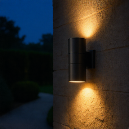 Black up down LED wall sconce on a stone garden wall at night
